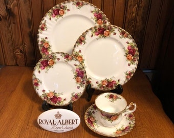 May include: A set of Royal Albert Old Country Roses bone china dinnerware, including a teacup and saucer, a bread and butter plate, a salad plate, and a dinner plate. The plates feature a floral pattern with roses, leaves, and gold trim.