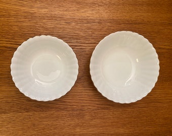 May include: Two white ceramic bowls with a scalloped edge. The bowls are empty and have a glossy finish.
