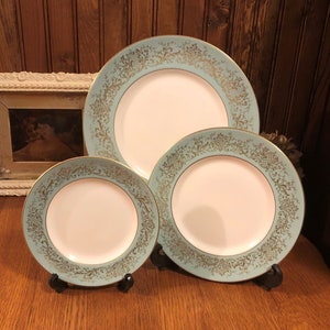 May include: Set of three vintage ceramic plates with a light blue and gold floral design. The plates are displayed on black stands.