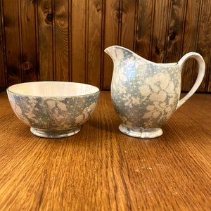 May include: A white creamer and sugar bowl set with a blue and white lace pattern.