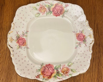 May include: A white square serving plate with a scalloped edge and a floral design featuring pink and yellow roses. The plate has a white background with a light pink polka dot pattern.