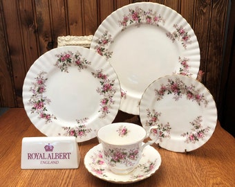 May include: A set of Royal Albert Old Country Roses fine china dinnerware, including a teacup and saucer, a bread and butter plate, a dinner plate, and a charger plate. The plates feature a delicate floral pattern with pink roses and green leaves.
