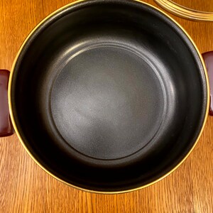 May include: A black pot with a gold rim. The pot is empty and has a smooth, black interior.