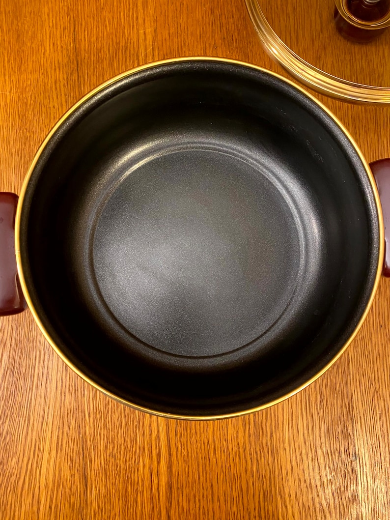 May include: A black pot with a gold rim. The pot is empty and has a smooth, black interior.