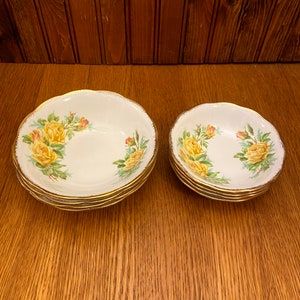 May include: A set of two white porcelain bowls with a yellow rose pattern and gold trim. The bowls are stacked on top of each other.
