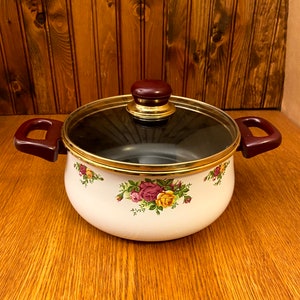 May include: White enamel pot with a glass lid and brown handles. The pot has a gold rim and a floral design with pink, yellow, and green roses.