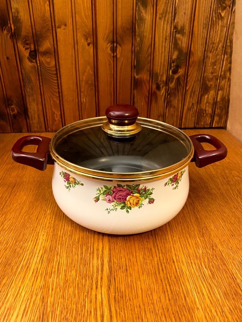 May include: White enamel pot with a glass lid and brown handles. The pot has a gold rim and a floral design with pink, yellow, and green roses.