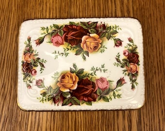 Può includere: Un piatto quadrato in ceramica bianca con un bordo dorato. Il piatto presenta un motivo floreale con rose rosse, gialle e rosa.