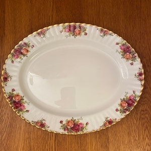 May include: A white oval serving platter with a gold rim and a floral pattern of red, pink, and yellow roses. The platter is on a wooden surface.