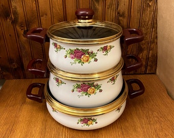 May include: A set of three white enamel saucepans with gold trim and a floral pattern. The saucepans have red handles and lids with glass tops.