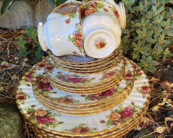 May include: A set of vintage teacups and saucers with a floral pattern and gold trim. The cups and saucers are stacked on top of each other and are surrounded by green foliage.