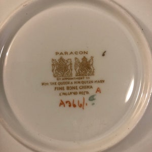 May include: A white porcelain saucer with a gold Paragon logo and the text "By Appointment to HM The Queen & HM Queen Mary Fine Bone China England Recd. A366/ A".