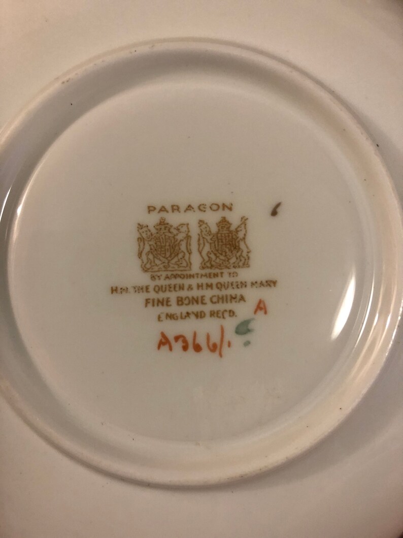 May include: A white porcelain saucer with a gold Paragon logo and the text "By Appointment to HM The Queen & HM Queen Mary Fine Bone China England Recd. A366/ A".
