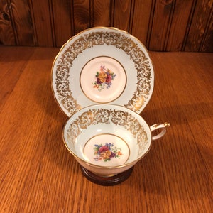 May include: A light blue teacup and saucer set with a gold trim and floral design. The cup and saucer have a delicate, ornate pattern.