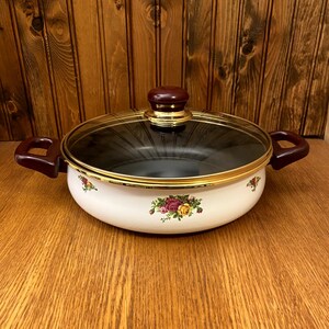 May include: White enamel saucepan with a floral design and a glass lid. The lid has a brown knob.