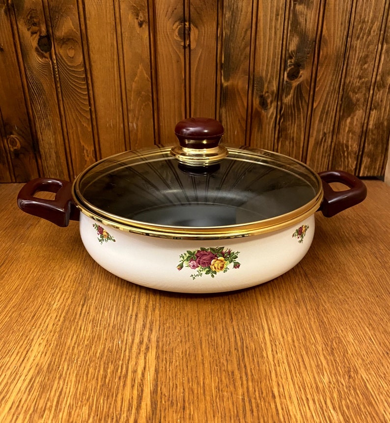May include: White enamel saucepan with a floral design and a glass lid. The lid has a brown knob.