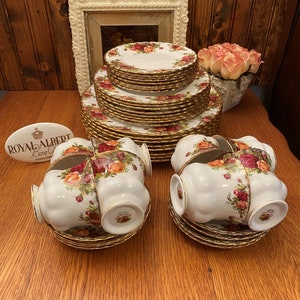 Puede incluir: Un juego de tazas y platillos de té de porcelana fina Royal Albert Old Country Roses. El juego incluye una pila de platos con un borde dorado y un patrón floral.
