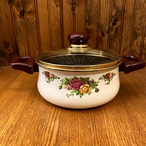 May include: White enamel pot with a gold rim and a glass lid. The pot has a floral design with pink, yellow, and green roses. The lid has a burgundy knob.