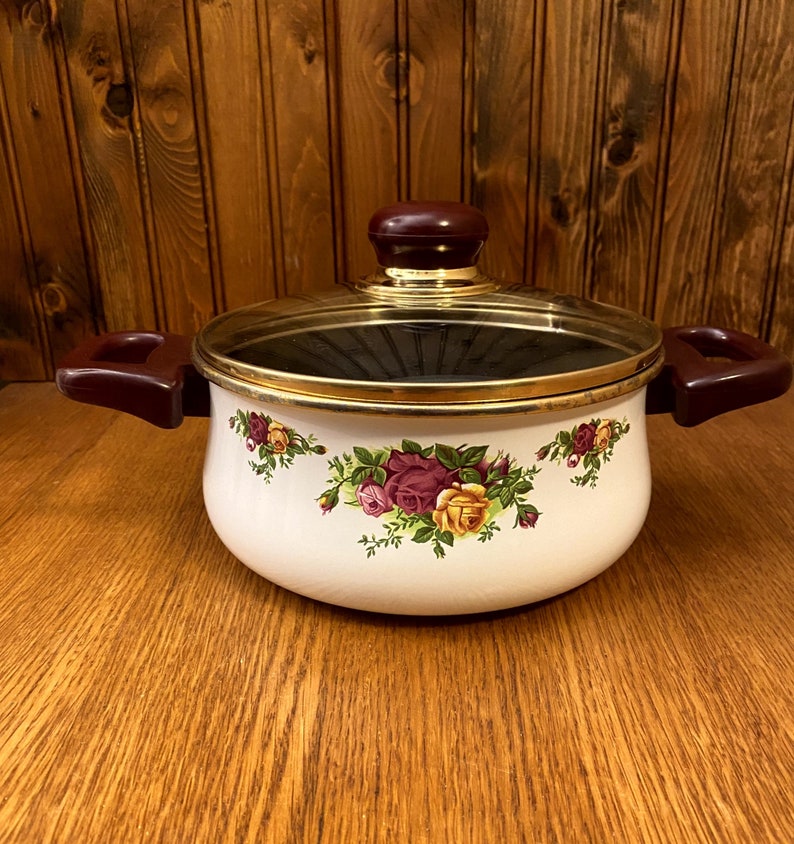May include: White enamel pot with a gold rim and a glass lid. The pot has a floral design with pink, yellow, and green roses. The lid has a burgundy knob.