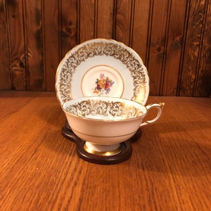 May include: A white teacup and saucer with gold trim and floral pattern. The saucer has a scalloped edge.