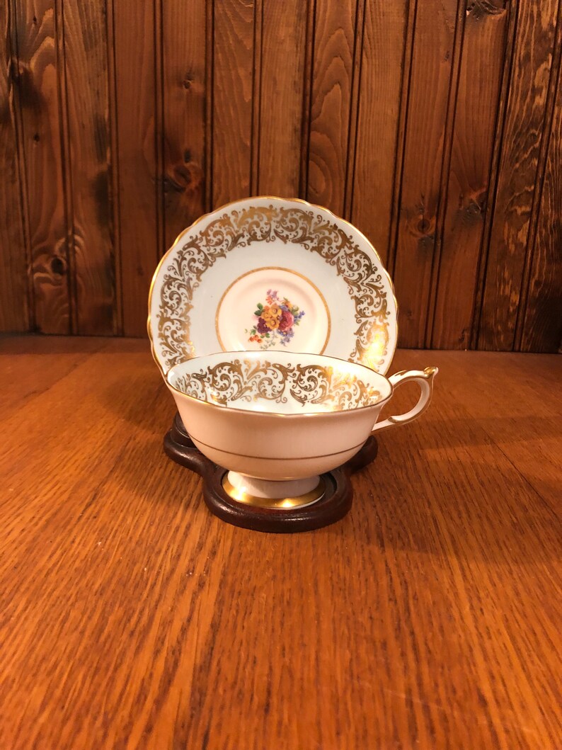 May include: A white teacup and saucer with gold trim and floral pattern. The saucer has a scalloped edge.