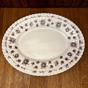 May include: Two white oval serving platters with a scalloped edge. The platters are decorated with a purple and green floral pattern.