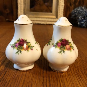 May include: A pair of white ceramic salt and pepper shakers with a gold trim and a floral design. The shakers feature a red rose pattern.
