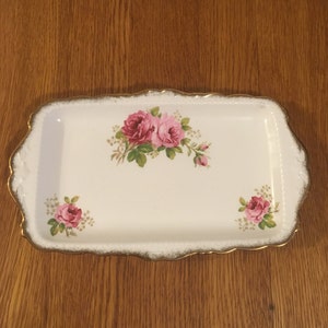May include: A white rectangular serving tray with a gold rim and a floral design featuring pink roses.