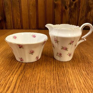 May include: A white porcelain creamer and sugar bowl set with a delicate pink rose pattern.