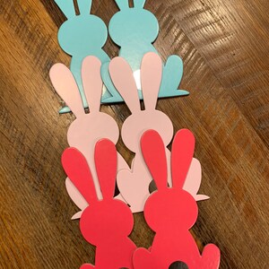 May include: Six cutout bunny shapes in three colors: light blue, pink, and red. The bunnies are stacked on top of each other, with the light blue bunnies on top, the pink bunnies in the middle, and the red bunnies on the bottom.