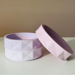 Könnte beinhalten: Zwei lilafarbene Silikon-Schalen mit einem strukturierten, rautenförmigen Muster. Die Schalen sind übereinander gestapelt.