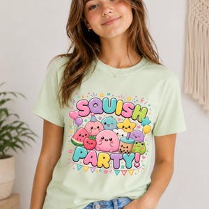 Może przedstawiać: Jasnozielony t-shirt z kolorowym nadrukiem graficznym z napisem "SQUISH PARTY!" otoczonym przez różne urocze, okrągłe postacie z kreskówek w pastelowych kolorach, w tym truskawkę, kawałek arbuza, gwiazdkę i kubek herbaty boba.