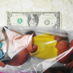 Puede incluir: Un animal de peluche marr&oacute;n y amarillo en una bolsa de pl&aacute;stico transparente. El juguete tiene un sombrero verde y azul.
