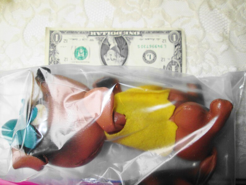 Puede incluir: Un animal de peluche marr&oacute;n y amarillo en una bolsa de pl&aacute;stico transparente. El juguete tiene un sombrero verde y azul.