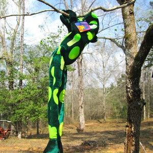 Pu&ograve; includere: Un grande rana di peluche verde e nero appeso a un ramo d'albero. La rana ha un motivo a macchie ed &egrave; appesa a testa in gi&ugrave;.