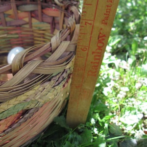 May include: A woven basket with a colorful pattern, filled with eggs, is measured with a wooden ruler marked "Rainbow Paint" up to 7 inches.