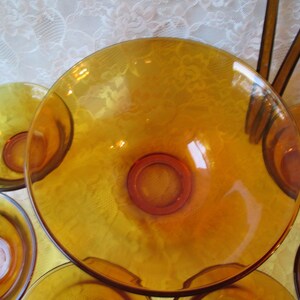 Peut inclure: Ensemble de bols de service en verre ambr&eacute;. Les bols sont ronds avec une base centrale sur&eacute;lev&eacute;e et un bord large et peu profond. Le verre a une finition brillante, refl&eacute;tant la lumi&egrave;re. Les bols sont dispos&eacute;s sur une nappe en dentelle blanche.
