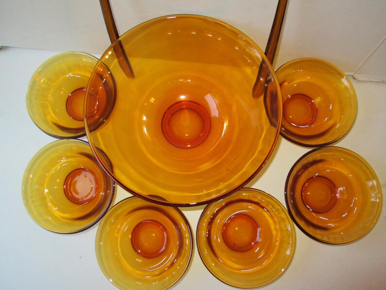 Peut inclure: Service de table en verre ambr&eacute;, comprenant un grand saladier et six petits bols. Les bols ont un design circulaire avec un centre sur&eacute;lev&eacute;. L'ensemble est id&eacute;al pour servir des collations ou des desserts.