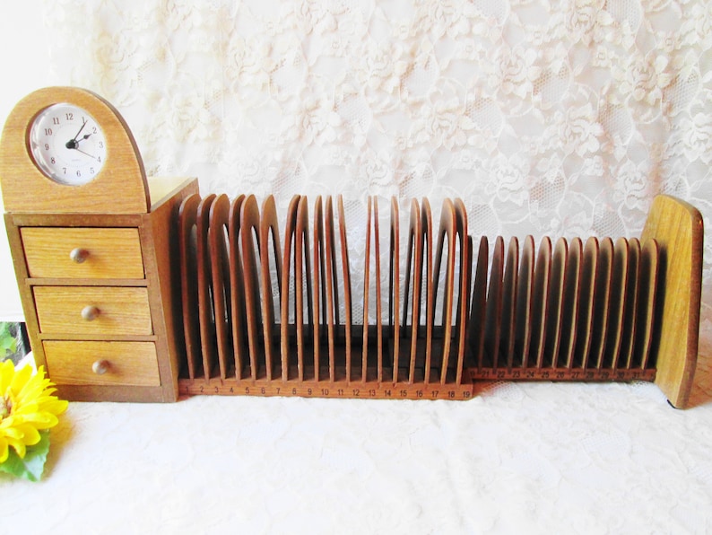 May include: A wooden letter holder with 19 slots and a small clock on top. The clock has a white face with black numbers and hands. The letter holder has a brown finish and is numbered 1-19.