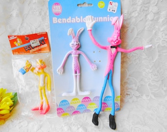 May include: A set of three bendable plastic toys. Two are pink and white bunnies with long limbs, and one is a yellow and pink bunny with a blue and white striped shirt. The packaging says "Bendable Bunnies" and "Egg Time".