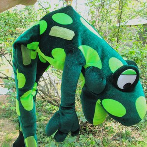 Pu&ograve; includere: Costume da rana di peluche verde con grandi occhi verdi e bianchi. La rana indossa un motivo a pois verde e bianco.