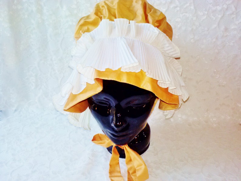 Puede incluir: Un gorro blanco y dorado con ribete de volantes. El gorro est&aacute; hecho de sat&eacute;n y encaje.