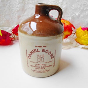 May include: A brown ceramic jug with a white label that reads "Pioneer Jug Daniel Boone 80 Proof Kentucky 1/4 Quart Straight Bourbon Whiskey Old Boone Distillery Co.  Pewee Valley, Kentucky".