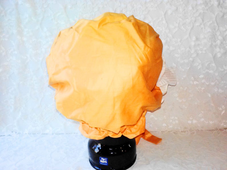 Puede incluir: Un gorro de ducha de tela de color naranja brillante con un ribete de encaje blanco. El gorro est&aacute; sobre una superficie blanca.