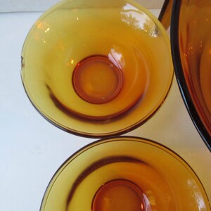 Peut inclure: Un ensemble de bols en verre de couleur ambre. Les bols ont une forme arrondie avec un centre ambre plus fonc&eacute;. Les bols sont probablement vintage et adapt&eacute;s pour servir des aliments. Le verre a une finition brillante.