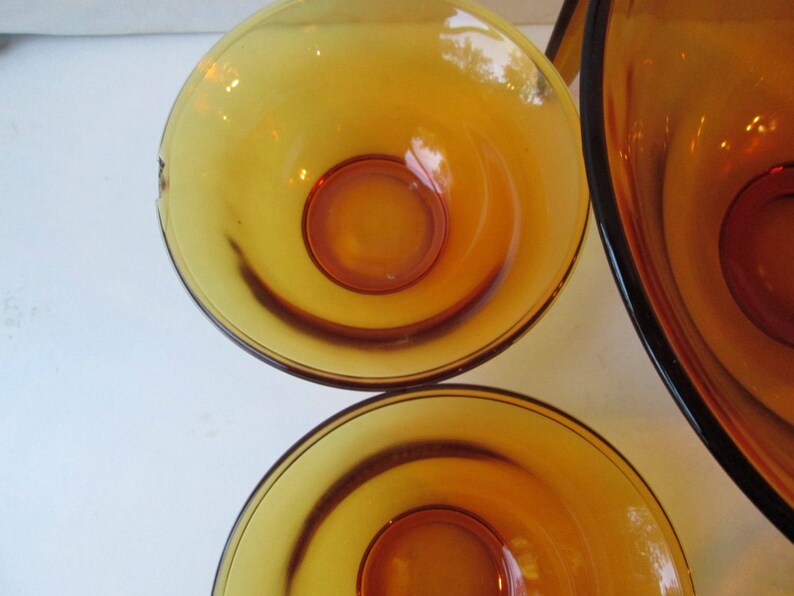 Peut inclure: Un ensemble de bols en verre de couleur ambre. Les bols ont une forme arrondie avec un centre ambre plus fonc&eacute;. Les bols sont probablement vintage et adapt&eacute;s pour servir des aliments. Le verre a une finition brillante.