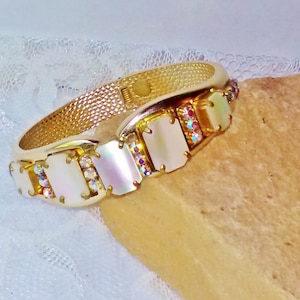 May include: A gold bangle bracelet with a row of iridescent rectangular stones and clear rhinestones.
