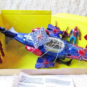 May include: A blue and red plastic toy helicopter with a spider web design. The helicopter is in a yellow box with a Spider-Man figure and instructions. The box says "The Amazing Spider-Man Web Copter".
