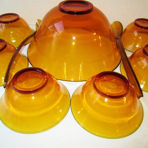 Peut inclure: Un ensemble de service en verre ambr&eacute; vintage, comprenant un grand saladier, six petits bols et deux cuill&egrave;res de service. Les bols et les cuill&egrave;res ont une teinte ambr&eacute;e chaude et transparente.