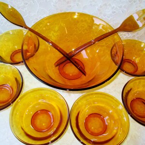 Peut inclure: Un ensemble de saladiers vintage en verre ambr&eacute;. L'ensemble comprend un grand saladier, six petits bols et deux cuill&egrave;res &agrave; salade. Les bols et les cuill&egrave;res ont une teinte jaune-dor&eacute;, id&eacute;ale pour servir des salades.